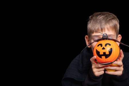 A child holding an orange pumpkin-shaped basket with a grinning face, Jacks lantern and a bat Trick or treat traditionの写真素材