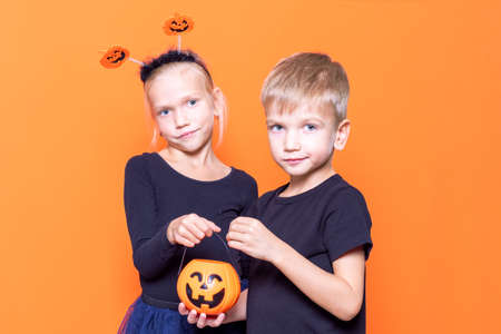 Childrens trick or treat is a Halloween tradition. Boy and girl holding an orange pumpkin-shaped basket with treatsの写真素材