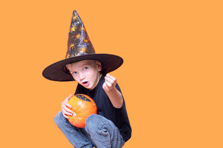 Halloween kids. Little Emotional boy in a wizard hat holding an orange pumpkin in his hands and showing a candyの写真素材