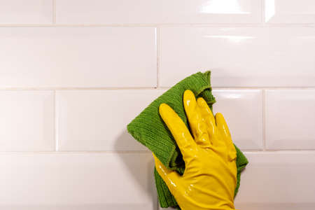 Hand in a yellow rubber glove wiping the ceramic tile surface with a green rag. Disinfection of the kitchenの写真素材