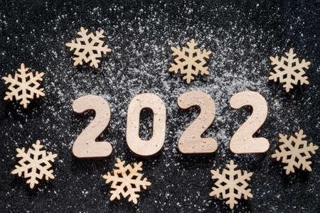 New Years concept - Wooden snowflakes and numbers 2022 sprinkled with snow on black glittering starry background. New Year card.の写真素材