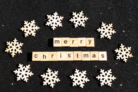 Wooden snowflakes and the inscription HAPPY CHRISTMAS from wooden letters on black shiny background