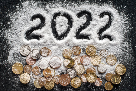 Hand written year 2022 and various coins covered with white sea salt such as snow on black...