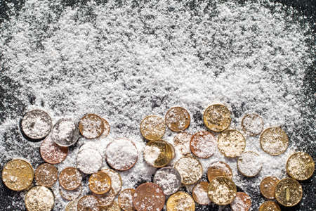 Coins covered with white sea salt such as snow on a black background. The concept of wealth and successの写真素材
