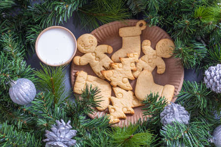 Christmas cookies, gingerbread cookies and a glass of milk in a craft glass for Santa with fir...