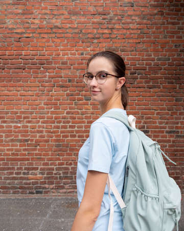 Portrait of a girl student in a T-shirt and with a blue backpack on a background of a brown brick wall. Student tourismの写真素材