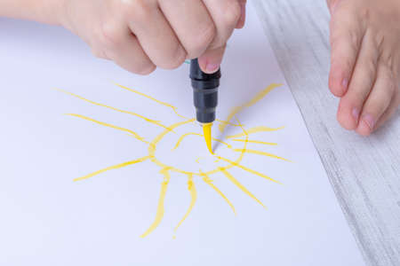 Childrens hands are drawing with a felt-tip pen, a pen a happy yellow sun on paper. Fun home schooling conceptの写真素材