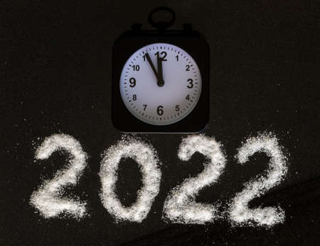 Classic black alarm clock showing the time 23:55 and the year 2022 written with white salt like snow on a black background. 12 hours. New Years Eve concept.の写真素材