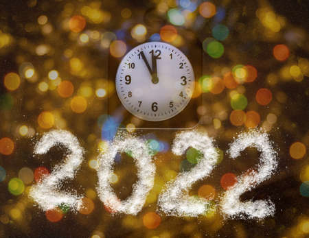 Classic alarm clock showing the time 23:55 and the year 2022 written with white salt like snow on a bright festive gold background with bokeh. 12 hours. New Years Eve concept.の写真素材