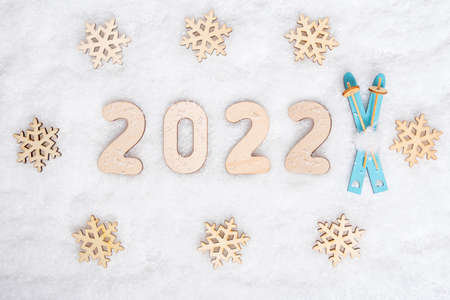 Sports year 2022. Bright blue wooden ski toys, snowflake shape and date 2022 on white snow, flat lay, copy space.の写真素材