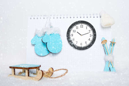 Time for winter rest. Round analog clock, toy wooden blue skis, sledges, mittens and white hat on...