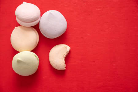 Round multi-colored marshmallows in a pile and one bitten half of a marshmallow on a red backgroundの写真素材