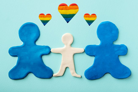 Two blue plasticine identical men as same-sex parents hold a white plasticine child on a blue background with rainbow heartsの写真素材
