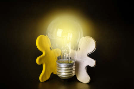 Two plasticine men holding a lit light bulb on a black background. Teamwork concept. Creative new idea. Innovation, brainstorming, inspiration and solution conceptsの写真素材