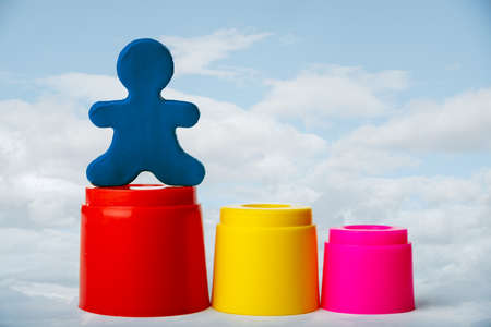 A plasticine man standing on the highest podium against a blue sky with clouds. Leadership concept.