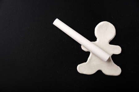 A small white plasticine man holding a chalk on a black board, copy space. Business concept....