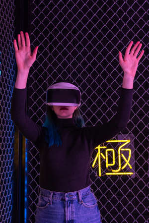 Teen girl using vr headset is in virtual reality cyberspace futuristic neon colorful background. The concept of the metaverseの写真素材