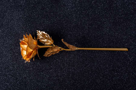 Beautiful handmade metallic golden rose flower with leaves and stem on a black background with shiny bokeh, close-up. Stylish trendy handmade decor. black and gold trendの写真素材