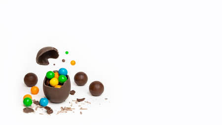 Cracked chocolate easter egg with colorful small round candies and chocolates on white background