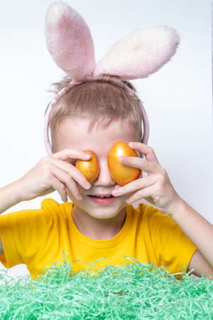 Portrait of a little blond boy covering his eyes with colorful eggs, close-up, vertical frame....