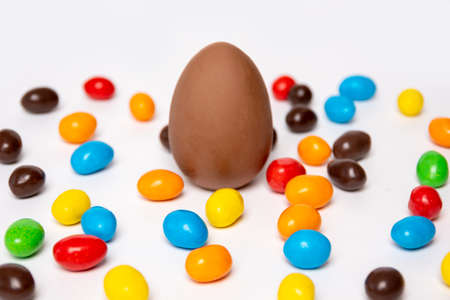 A whole chocolate egg on a white background with colorful candies. Treats for children. Sweet dessert for kids. Sweet Easter tradition.の写真素材