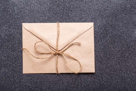 Closed brown craft envelope tied with twine with a bow on a black background. An envelope for your congratulations. Zero waste concept.の写真素材