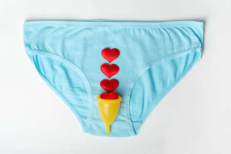 Womens blue panties, underwear and a yellow menstrual cup with red hearts shape as menstrual drops...