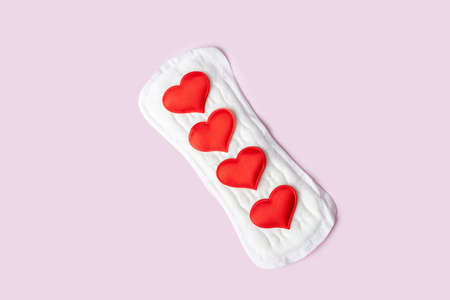 White cotton daily sanitary pad and red hearts as mestrual drops on pastel pink background, top view, flat lay, minimalism. Menstrual cycle. Womens hygiene and health care.の写真素材