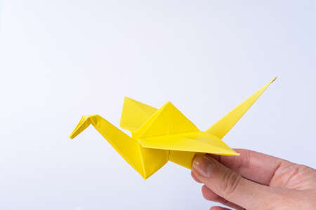 A hand holding a paper yellow bird on a light background. Paper crane as a symbol of peace. paper origami. paper crafts with children.の写真素材