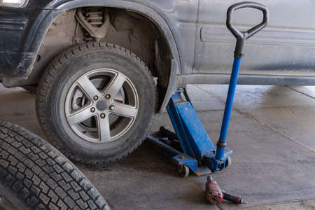 Jacking up a car to change a tyre after a roadside puncture with the jack inserted under the...
