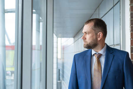 A smart, serious, confident Arab businessman looking out the window at the street. Portrait of a handsome middle-aged businessman in a suit. The concept of career and entrepreneurship.の写真素材