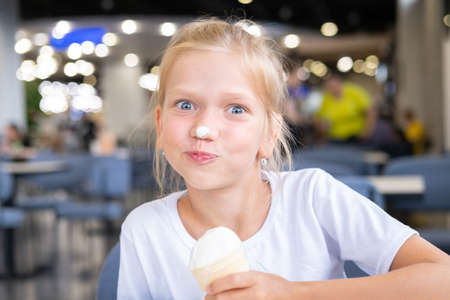 Portrait of a little hungry funny girl eating cold delicious ice cream in a waffle cup sitting in a...