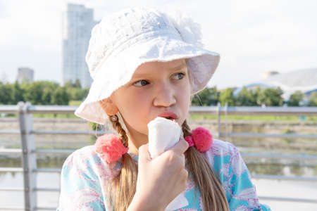 Hungry kid eating street food on the beach in summer. A girl in a hat eating fried sausages. Happy...