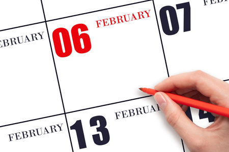 6th day of February. A hand holding a red pen and pointing on the calendar date February 6. Red calendar date, copy space, mockup. Winter month, day of the year concept.の写真素材