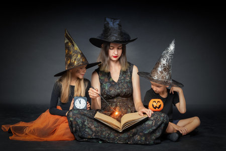 Family Halloween. A happy family in creepy costumes of witches and wizards, holding a large book with predictions, pumpkin-shaped baskets, a black watch and a magic wand on a black backgroundの写真素材