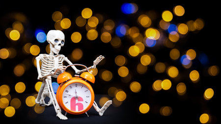 A human skeleton waving his hand, greeting holding an orange alarm clock on a black background, bokeh. Its Halloween time. Greeting cardの写真素材