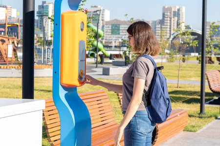 A student girl with a backpack presses the emergency terminal help button on a city street. The girl...
