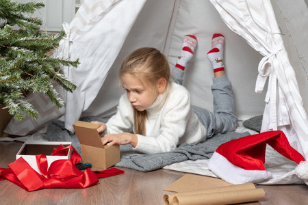 Family Christmas. Kids opening Xmas presents. Cute little girl is opening a present and smiling while sitting on the floor at homeの写真素材