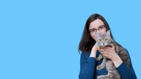 A cheerful student girl hugging a naughty gray striped kitten on a blue background, banner, copy...