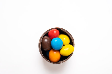 Cracked chocolate easter egg with colorful small round candies on white background, copy space, top...