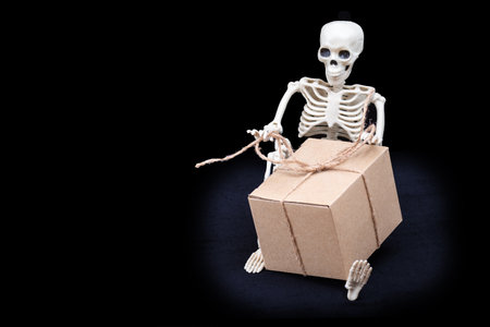 Skeleton holding a gift box on a black background. Gift for the day of the dead. Halloween shopping.