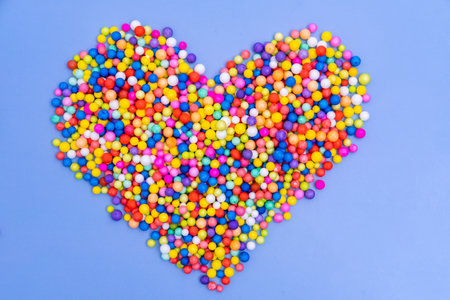 A large heart of bright multicolored round candies, dragees on a blue background. Sugar candies. A fun holiday. Childrens sweets. Favorite food. Sweet Valentine Cardの写真素材