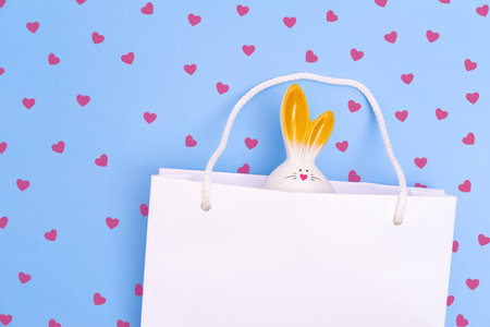 Shopping for Easter. White paper shopping bag with white bunny on blue background with red hearts. Concept Easter gifts, preparation, holiday surprise.の写真素材