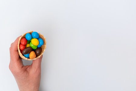 A hand holding an empty waffle cone with scattered multicolored round candies, dragees. A fun...