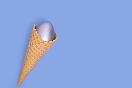 Waffle ice cream cone with decorated silver Easter egg on a blue background, concept, copy space,...