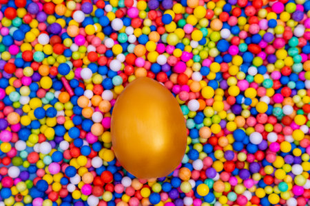 Painted Easter golden egg on a background of Bright multicolored round candies. Sweet Easter. A fun...