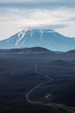 Road to volcano, snowy mountain through dark lava-covered ground and volcano craters. Journey to the land of volcanoes. mountain hiking. Russia, Kamchatka.の写真素材