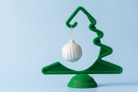 Creative little green Christmas tree with a hanging silver ball on a blue background, minimalism....