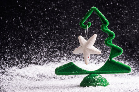 Creative little green Christmas tree with a hanging white star on a black snowy background, minimalism. Waiting for a miracle. New Year and Christmas cardの写真素材