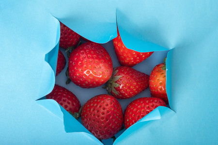 Blue background with a hole with red strawberries. Strawberry background. Red fresh strawberry wallpaper. natural food. Vegetarianの写真素材